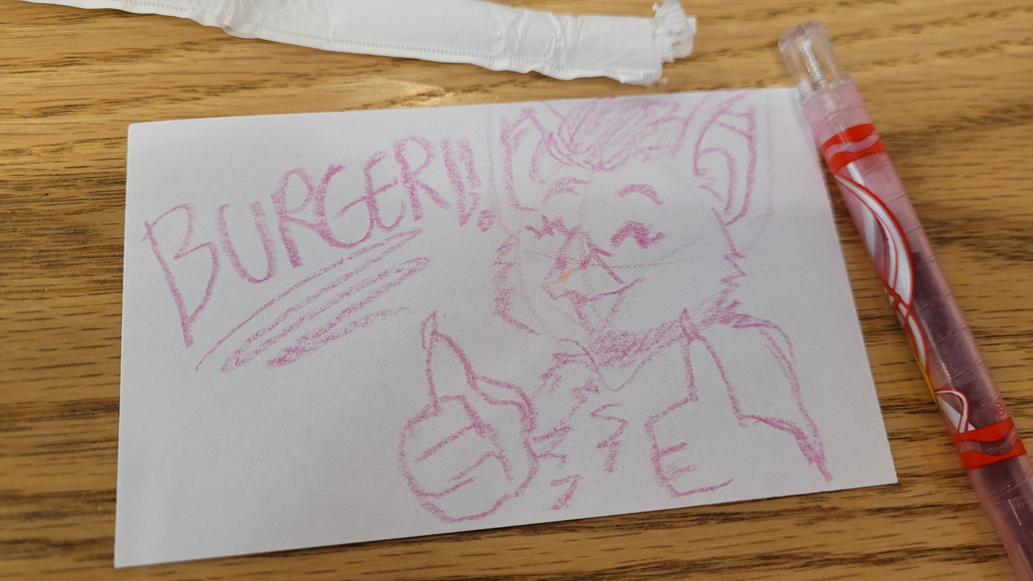A drawing of an anthro vampire bat drawn on cardstock with a crayon, with writing that reads 'BURGER!!' beside the bat